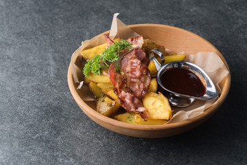 Fried potatoes with appetizing bacon and sauce are in a wooden plate