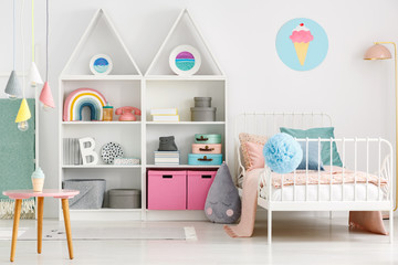 White kid's room interior with a single bed, rainbow on the shelf, pompom and ice cream poster on the wall