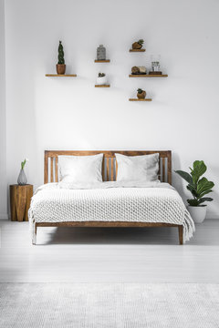 Wooden framed double bed with two pillows and a blanket, and small shelves above in a white bedroom interior. Real photo.