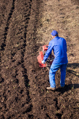 Worker with a machine cultivator digs the soil in the garden