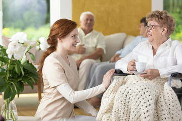 Obraz premium Smiling nurse taking care of disabled senior woman in the nursing house