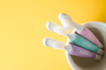 Close-up three white plastic toothbrushes in white mug on yellow background, Selected focus
