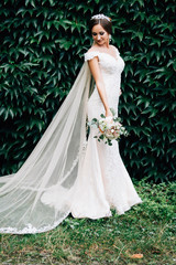 Portrait of a bride in a white dress with a wedding bouquet in the hands, against a background of a green wall of plants