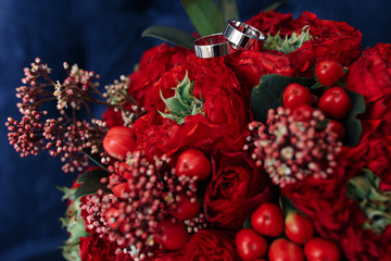 Classic white gold wedding rings on red bouquet, horizontal shot