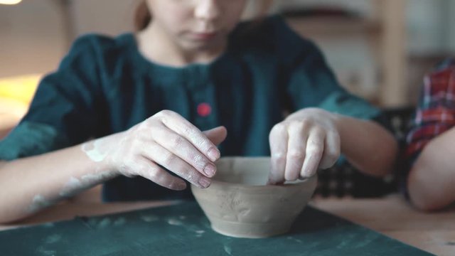child is making a plate of clay. a lesson in pottery. little girl makes patterns on a clay stamp