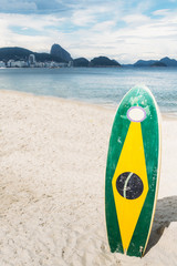 Longboard surfboard with a Brazilian flag standing on the sand overloooking the coastline of...