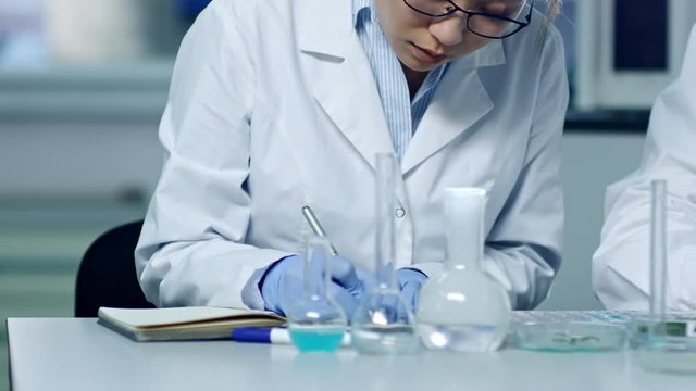 Close up shot of three chemists writing down information about research results and studying plant specimens in laboratory, tracking right