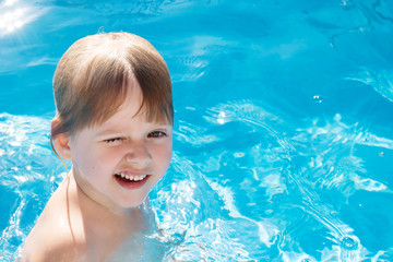 a little laughing blonde girl is swimming in the pool with clear blue water outdoors. copyspace.