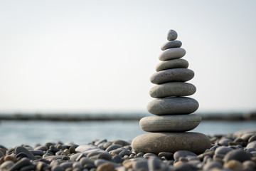 a pyramid of stones on a pebble beach against the sea and sky.