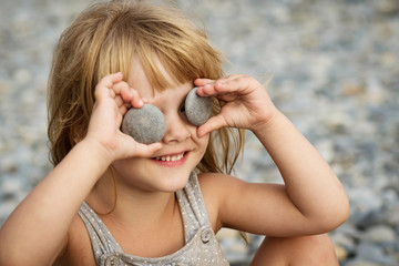 little girl closes her eyes with stones sitting on the pebble beach