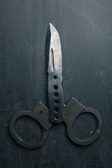 Metal handcuffs and tactical knife on dark background,