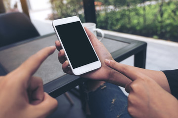 Mockup image of two people looking and pointing at a white mobile phone with blank black desktop screen in cafe