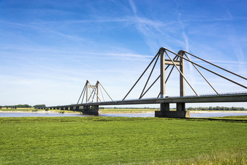 Fototapeta na wymiar Dutch landscape with bridge over the river Waal in the Netherlands, with blue sky and green meadows