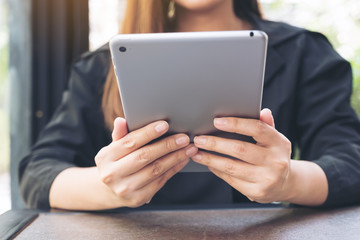Closeup image of a woman holding and using tablet pc in modern cafe