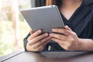 Closeup image of a woman holding and using tablet pc in modern cafe