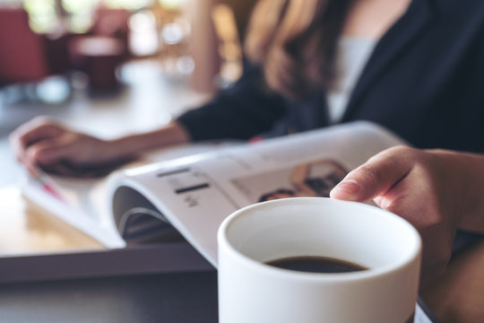Closeup image of a business woman reading a book while drinking coffee in cafe