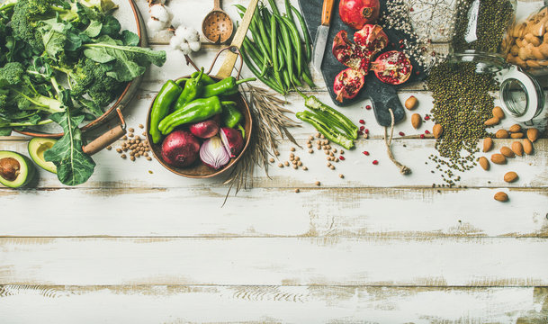 Winter vegetarian, vegan food cooking ingredients. Flat-lay of vegetables, fruit, beans, cereals, kitchen utencil, dried flowers, olive oil over white wooden background, top view, copy space