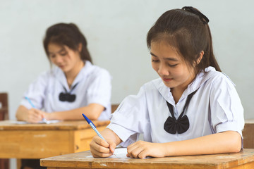 Students writing pen in hand doing exams answer sheets exercises in classroom with not stress.
