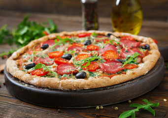 Pizza with salami, tomatoes, olives and cheese on a dough with whole wheat flour. Italian food.