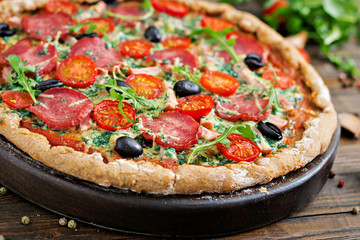 Pizza with salami, tomatoes, olives and cheese on a dough with whole wheat flour. Italian food.