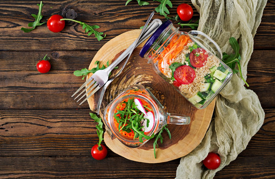 Salads with quinoa,  arugula, radish, tomatoes and cucumber in glass  jars on  wooden background.  Healthy food, diet, detox and vegetarian concept. Top view. Flat lay