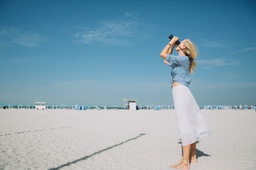 Beautiful natural blonde woman looking through binoculars against blue sky