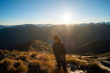 A young Asian man with sunglasses enjoying a stunning scenery of alps on the high mountain before sunset in a beautiful blue sky day.