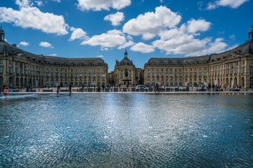 Fototapeta na wymiar Bordeaux, France, 10 may 2018 : Tourists visiting the Place de la Bourse seen from the boulevard with in front the mirror fountain: 'Mirroir d'eau'