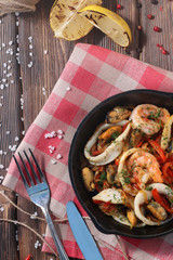 seafood in a frying pan vith catlery and garlic top view