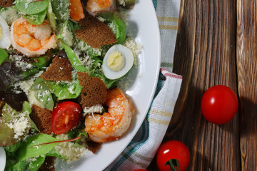 Caesar salad with shrimps and cherry tomato on wood background