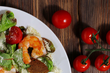 Caesar salad with shrimps and cherry tomato on wood background