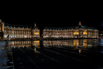 Bordeaux, France, 10 may 2018 - Tourists visiting the Place de la Bourse at night seen from the boulevard with in front the mirror fountain: 'Mirroir d'eau'