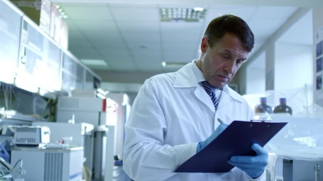 Medium shot of middle-aged male scientist writing important data related to his research on paper attached to clipboard