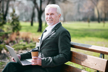 Fototapeta premium Warm weather. Enthusiastic mature businessman using laptop while drinking coffee