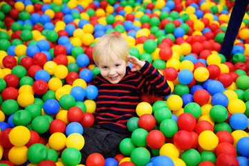 Fototapeta na wymiar Happy little boy having fun in ball pit with colorful balls