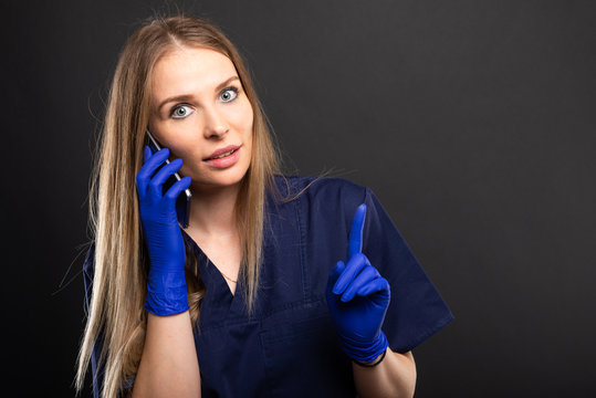 Female doctor wearing scrubs talking at smartphone gesturing.