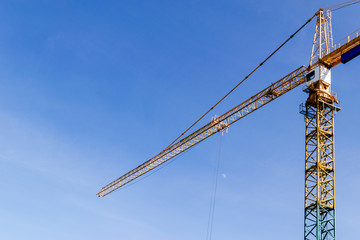 Naklejka premium Construction crane tower on blue sky background. Crane and building working progress. Yellow lifting faucet. Empty Space for text. Construction concept. Site. New buildings with a crane. Tower crane