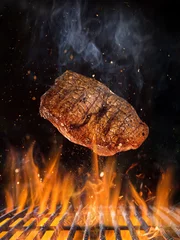 Plexiglas foto achterwand Tasty beef steak flying above cast iron grate with fire flames. © Lukas Gojda