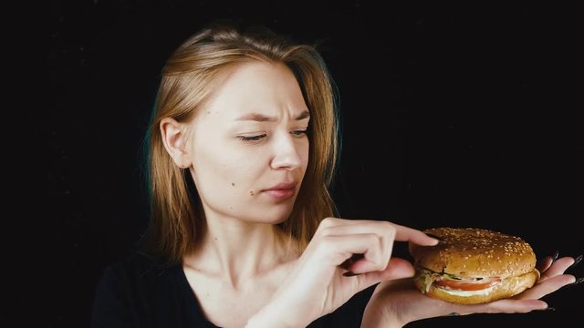 Bad hamburger. Poor food. The girl looks at the hamburger in disgust. Bad fast food.