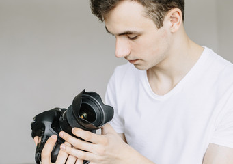 Fototapeta premium A young man holds a photo camera in his hand and looks at the lens in the dust, a dirty lens. Іsolated gray background