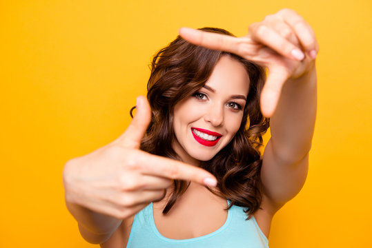 Portrait of pretty creative girl with beaming smile red pomade lipstick making frame with thumbs and forefingers looking at camera isolated on yellow background
