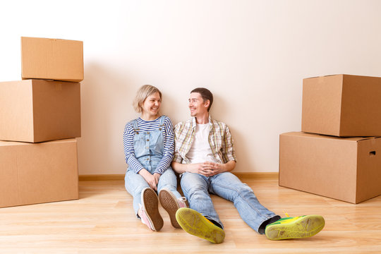 Photo of young married couple sitting on floor among cardboard boxes