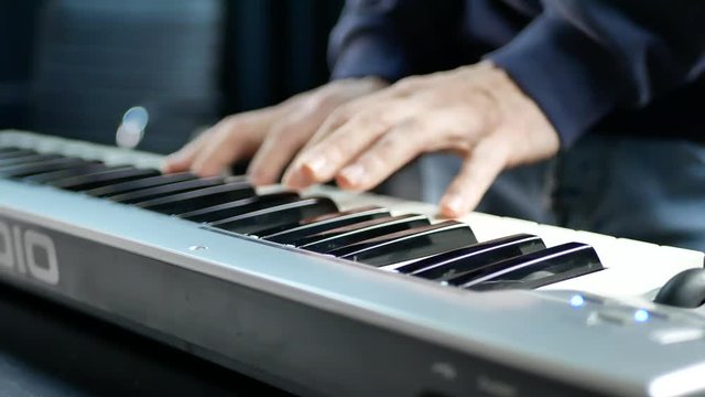 The pianist's hand plays on the electronic piano at the recording studio. White and black synthesizer keys