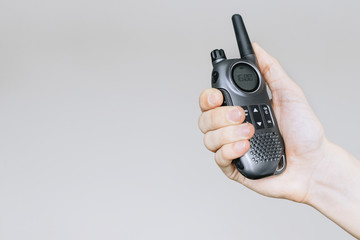 Holds a walkie-talkie in his hand on a gray background. Portable radio. Іsolated white background