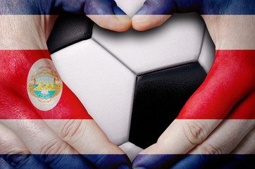 Hands painted with a Costa Rica flag forming a heart over soccer ball background