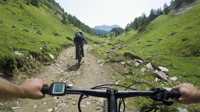 POV man riding e-bike following friend woman.Mtb action cyclist exploring together mountain trail path.Electrical bike active people sport travel vacation in Italy Alps outdoors in summer.4k video