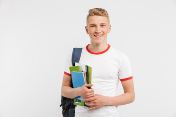 Image of european student boy wearing backpack smiling and looking at you with textbooks in hands, isolated over white background