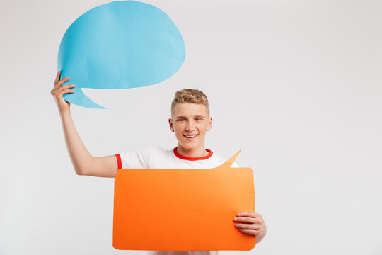 Photo of smiling advertiser boy wearing casual t-shirt holding two copyspace bubbles for your text, isolated over white background
