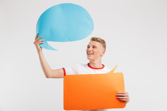 Photo of cheerful male teenager wearing casual t-shirt holding two copyspace banners for your text, isolated over white background - Powered by Adobe