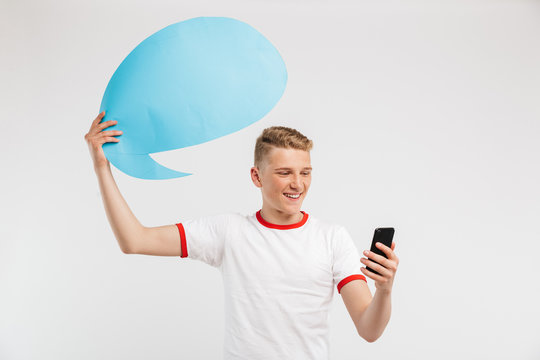 Photo of satisfied hipster boy holding commercial poster copyspace for your text above his head and using smartphone, isolated over white background